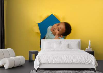 African-American boy on yellow background of torn paper shows positive hand sign, finger up or thumb up, gesture of approval or like, showing bursts of positive emotions. Concept of recommendation Wall mural