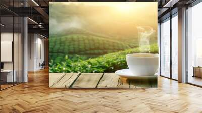 A cup of steaming tea sits on a wooden table with a breathtaking view of a misty green tea plantation at sunrise. Wall mural