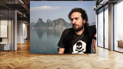 Young long-haired and bearded adult staring at the breath-taking landscape formed by rock formations at the Ha Long Bay, Vietnam. Wall mural