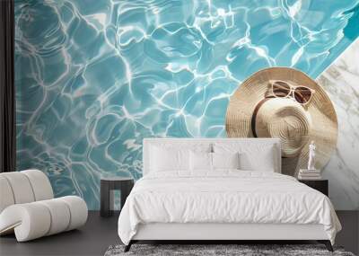 A minimalistic fashion aesthetic scene featuring sunglasses and a straw hat beside a marble swimming pool with clear blue water, highlighted by wave patterns and light reflections Wall mural