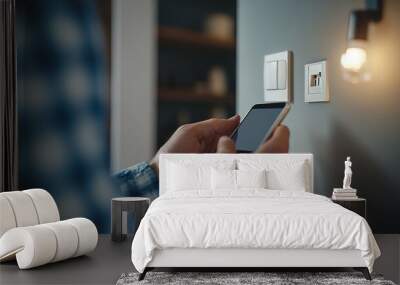 Close-up of a man pressing a light switch, with an electric socket, plug, and smartphone in view Wall mural