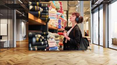 A woman is shopping for fabric in a store. She is wearing headphones and looking at the different colors and patterns of fabric Wall mural