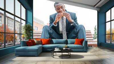 african-american man eating burger in a park outdoors while using his smartphone Wall mural