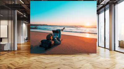 mature latin digital nomad laying on the sand of the beach with a laptop working at sunset over the ocean Wall mural