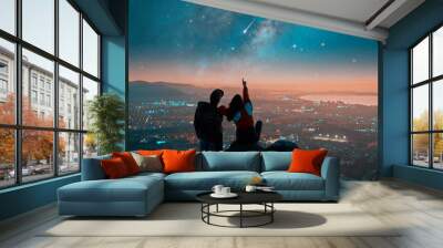 silhouettes of a couple sitting on the top of the mountain looking and pointing out at shooting star and milky way over the city lights on the horizon	 Wall mural