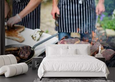 steaks grilling on open flame and chef hands slicing steak in background Wall mural