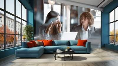 Diverse business team having a discussion in a meeting room. A group of professional people are talking at a table with a laptop and documents, working together on a project plan or making skills trai Wall mural