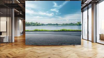 Empty asphalt road and green trees with blue sky background over the lake in summer, landscape nature view from side of empty street for product display. Wall mural