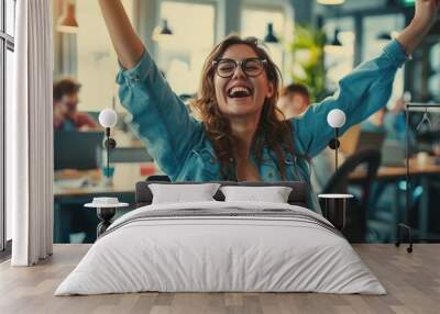 Startup young woman very happy and excited doing winner gesture with arms raised sitting on chair in office. Wall mural