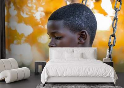 Close-up Portrait of a Young Boy with Dark Skin, Looking Down, Against a Blurred Yellow and White Background Wall mural