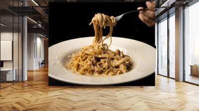 hand raising spaghetti with fork from white plate with alfredo sauce Wall mural