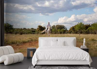 Young guy in casual outfit riding white horse on sandy road Wall mural