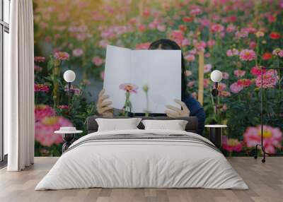 Female covering her face with blank book or magazine with zinnia flowers in a garden Wall mural