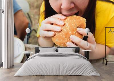 Close up of a young woman, wearing a yellow t shirt, eating an hamburger. Wall mural