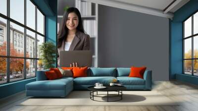 Beautiful Asian businesswoman using laptop computer while standing in the modern office room. Wall mural