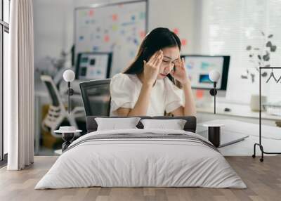 Businesswoman is feeling tired and having a headache after working on a laptop for too long, she is touching her temples and closing her eyes Wall mural