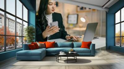 Businesswoman is working late, using her laptop and checking her smartphone to stay connected and on top of her tasks Wall mural