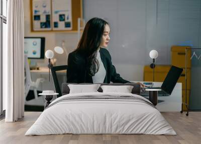 Dedicated businesswoman burning the midnight oil in the office, reviewing documents and typing on her laptop, fully immersed in her work Wall mural