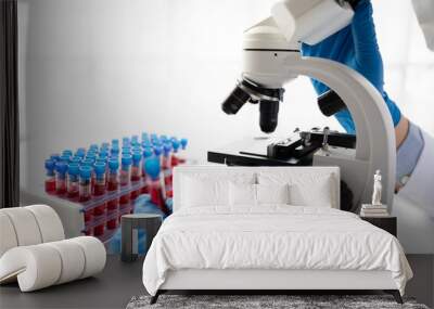 Doctor hand taking a blood sample tube from a rack with machines of analysis in the lab background, Technician holding blood tube test in the research laboratory. Wall mural