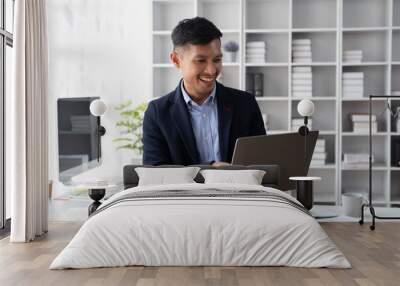 Happy mature buisnessman standing and typing on lapptop computer in his office room. Wall mural