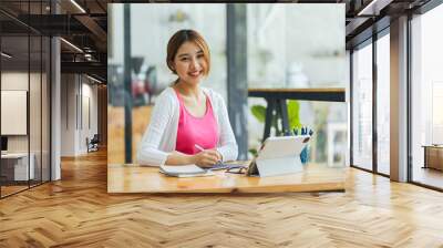 Portrait of smiling beautiful Asian business woman enjoy the idea sitting at office, Asian student girl look at laptop while doing homework making video call abroad using internet friend connection. Wall mural