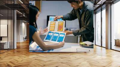 Two designers deeply engrossed in conversation about mobile app templates, analyzing user experience and interface elements in a modern office space Wall mural
