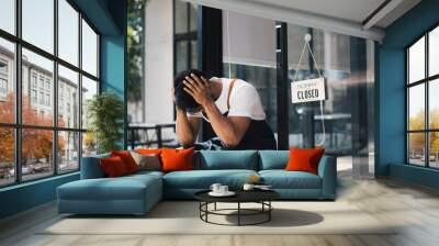 Young asian male coffee shop owner feeling stress or depress while sitting in front of his coffee shop. Wall mural