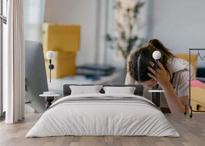 Young asian woman working in her home office is stressed out from work. She is surrounded by moving boxes and paperwork Wall mural