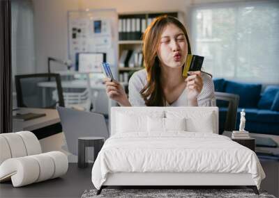 Young businesswoman is sitting at her desk and kissing her credit card while shopping online on her laptop. She is happy with her purchase Wall mural