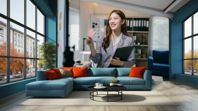 Young manager woman is holding a pen and clipboard while smiling and presenting a business idea on a board during a meeting in the office Wall mural