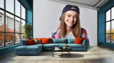 closeup portrait of smiling teen girl wearing checkered shirt and baseball cap, over grey background Wall mural