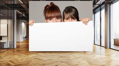 two young women peeking over edge of blank banner Wall mural