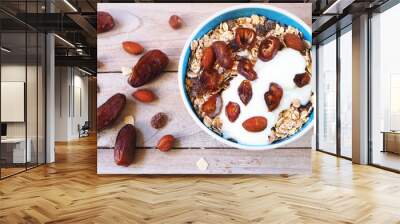 Top view of a healthy bowl of Muesli with whole grain, oats, dried fruit, nuts and date fruit with yogurt on a wooden table. Wall mural