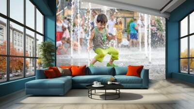 excited boy having fun between water jets, in fountain. Summer in the city Wall mural