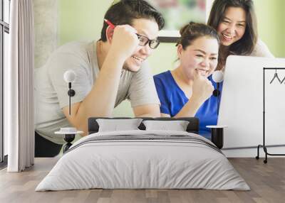 Two women and one man are happily looking at computer in modern office Wall mural