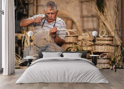 Senior Latin American man using hammer while doing wicker baskets at his workshop Wall mural