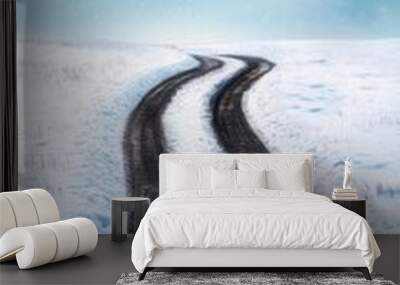 A winding road through a snow-covered landscape under a dramatic sky with clouds, creating a serene winter atmosphere. Wall mural