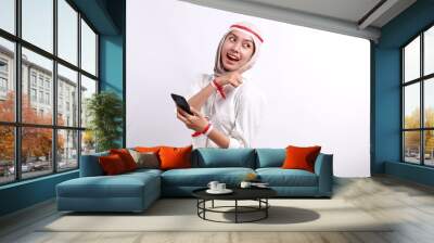 A happy Asian muslim woman with red white flag headband, holding her phone, and pointing copy space beside her, isolated by white background. Indonesia's independence day Wall mural