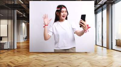 Excited young Asian woman with red white flag ribbon using mobile phone, getting good news isolated on white background. indonesian independence day celebration concept Wall mural