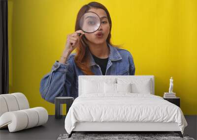 Funny asian woman standing while looking through magnifying glass. Investigation concept Wall mural