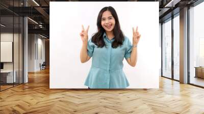 Positive successful Asian woman licks lips, makes victory gesture, shows two fingers, dressed in stylish shirt, poses indoor, rejoices success, isolated white background. Sign language Wall mural