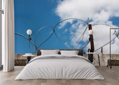 coils of barbed wire on the old concrete fence on blue sky background and white clouds. rusty beam Wall mural