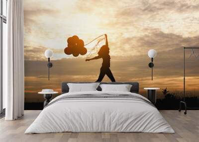 Silhouette of girl with balloons in the sunset background. Wall mural