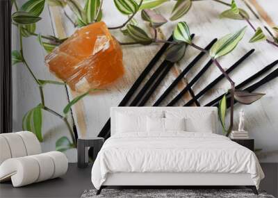 A close up image of honey calcite with several incense sticks and green plant on a white wooden background.  Wall mural