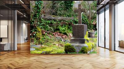 An image of a large stone cross weathered by time in a moss covered cemetery.   Wall mural