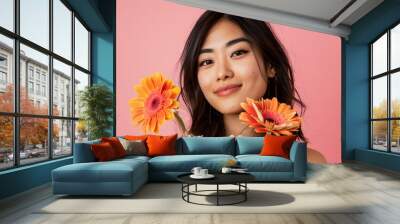 A portrait of a young adult and Asian woman holding flowers; Gerbera daisy, while smiling at the camera with an isolated pink background with copy space  Wall mural