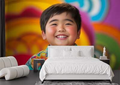 Chubby Asian boy smiling brightly in colorful studio, wearing vibrant floral shirt. His joyful expression adds warmth to lively background Wall mural