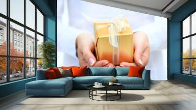 woman's hand with a small gold gift box with bow isolated on whi Wall mural