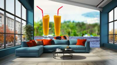 two glasses of mango cocktail juice and orange sunglasses on wood table. blue sea on the background. Wall mural