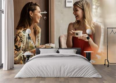 Beautiful happy women talking and laughing while drinking coffee together in coffee shop. Wall mural